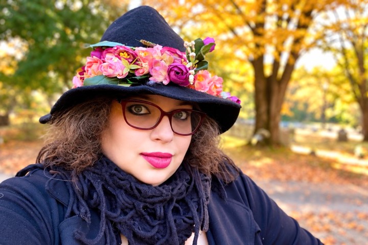 Person outdoors in fall, wearing glasses and a hat with flowers.