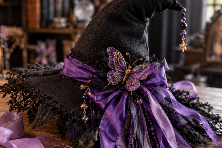 Decorated witch hat with purple ribbons and butterfly on a wooden table with sewing supplies.