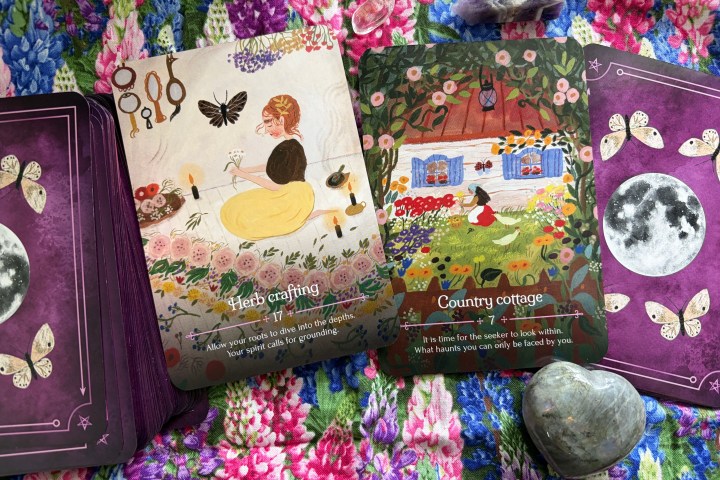 Two tarot cards on a floral quilt with crystals and a heart-shaped stone.