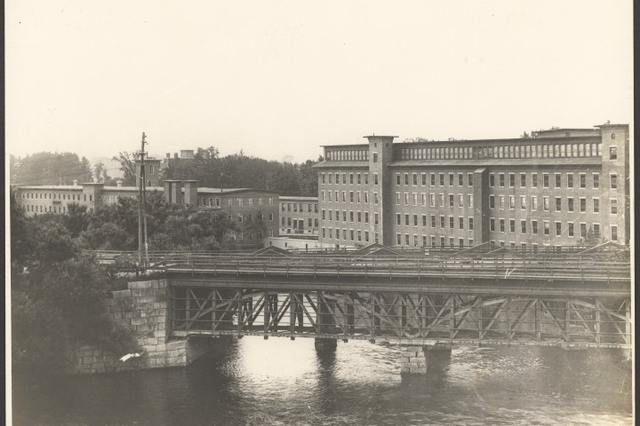 Historic brick buildings and an iron bridge over a river.