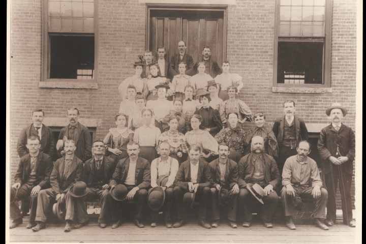 Vintage group portrait of men and women in front of a brick building.