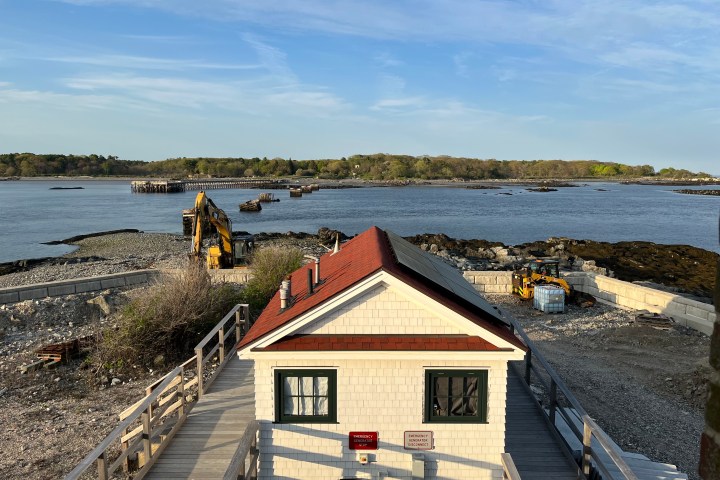 House with red roof by the sea, construction equipment in the background on a sunny day.