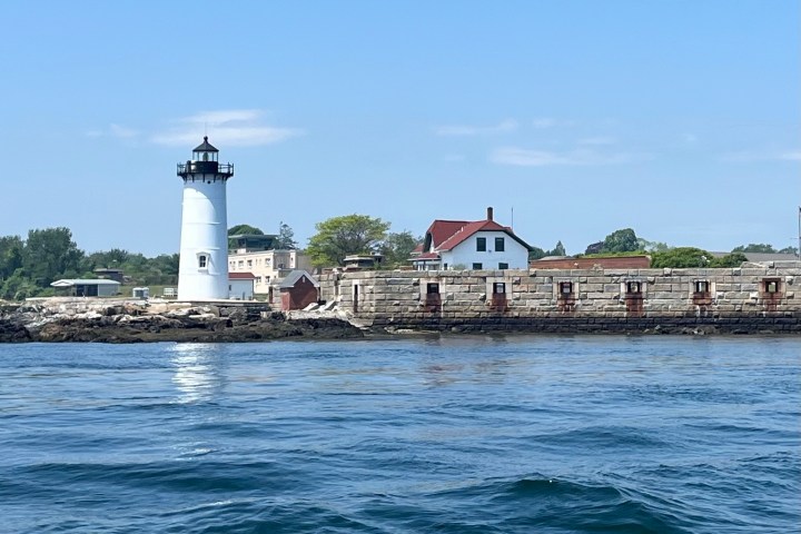 White lighthouse and buildings on rocky shore under clear blue sky.