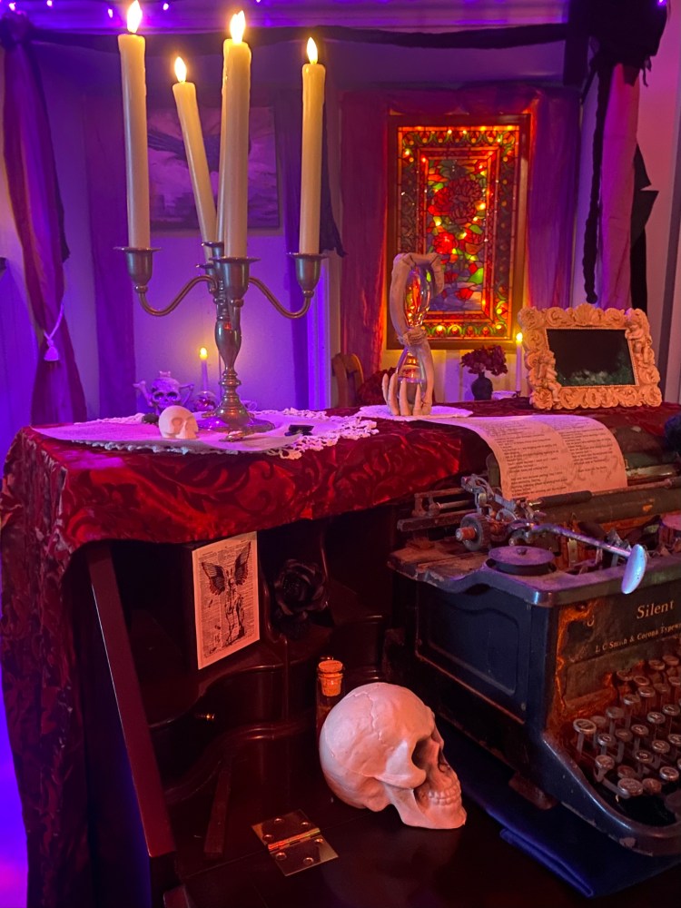 Candlelit gothic scene with a typewriter, skull and colorful stained glass window.