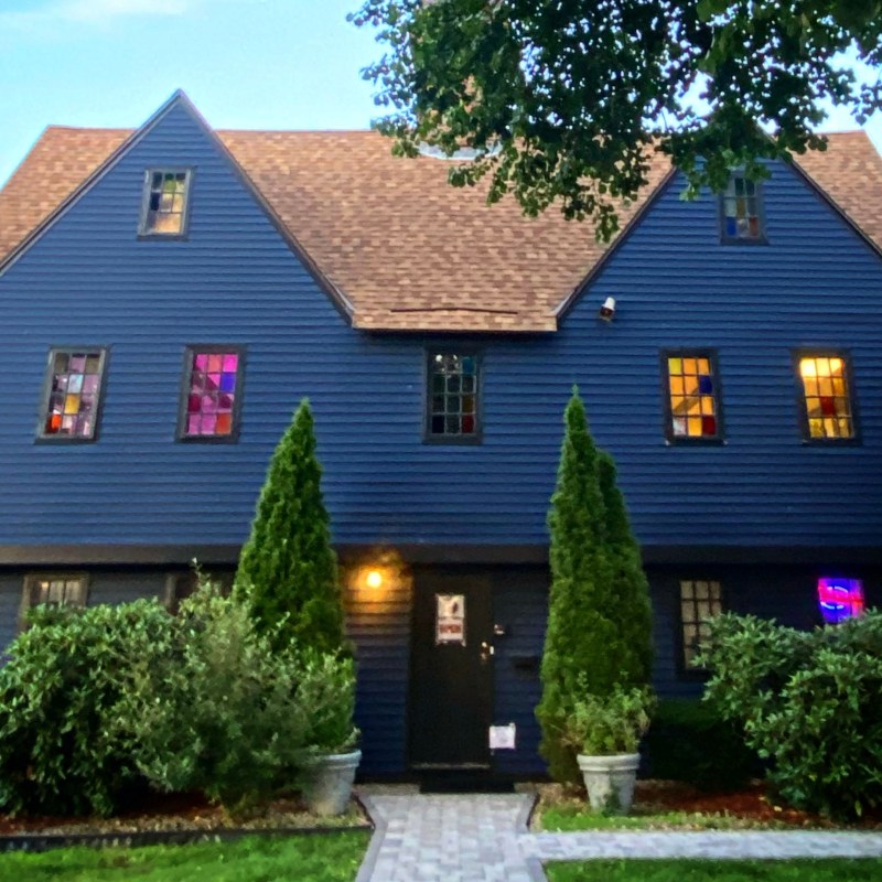 Dark blue house with steep roof, lit windows, and front shrubs.