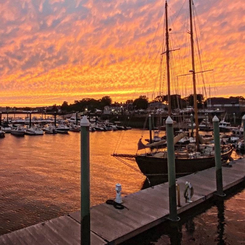 Sunset at a marina with a sailboat and vibrant orange sky.