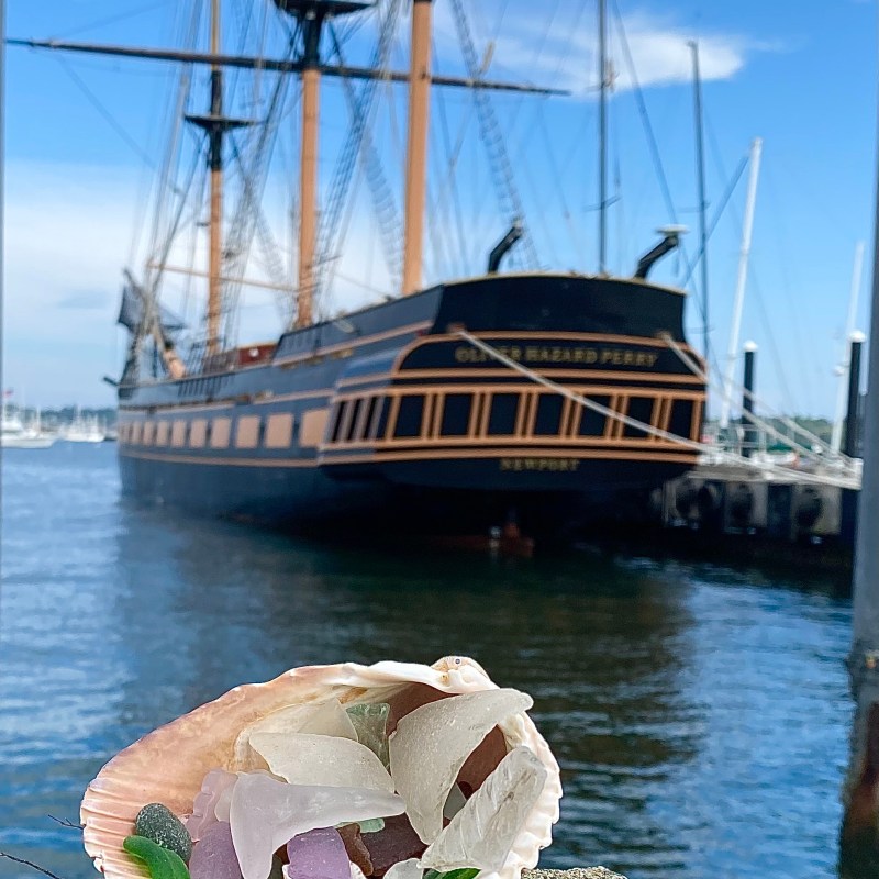 Shell with sea glass in foreground, historic ship docked in the background.