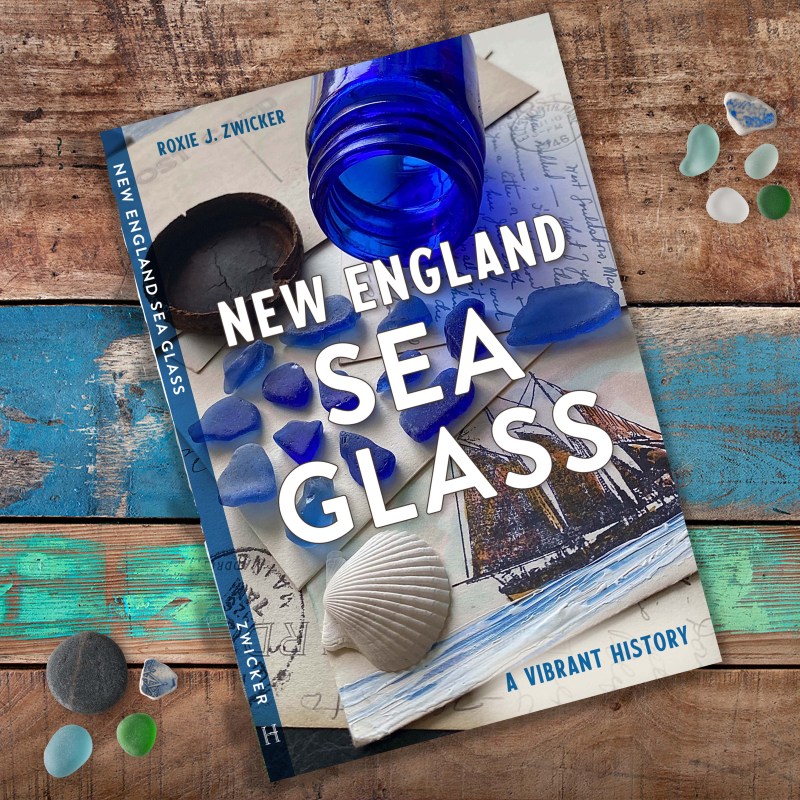 Book titled 'New England Sea Glass' on wooden background with sea glass and shells.