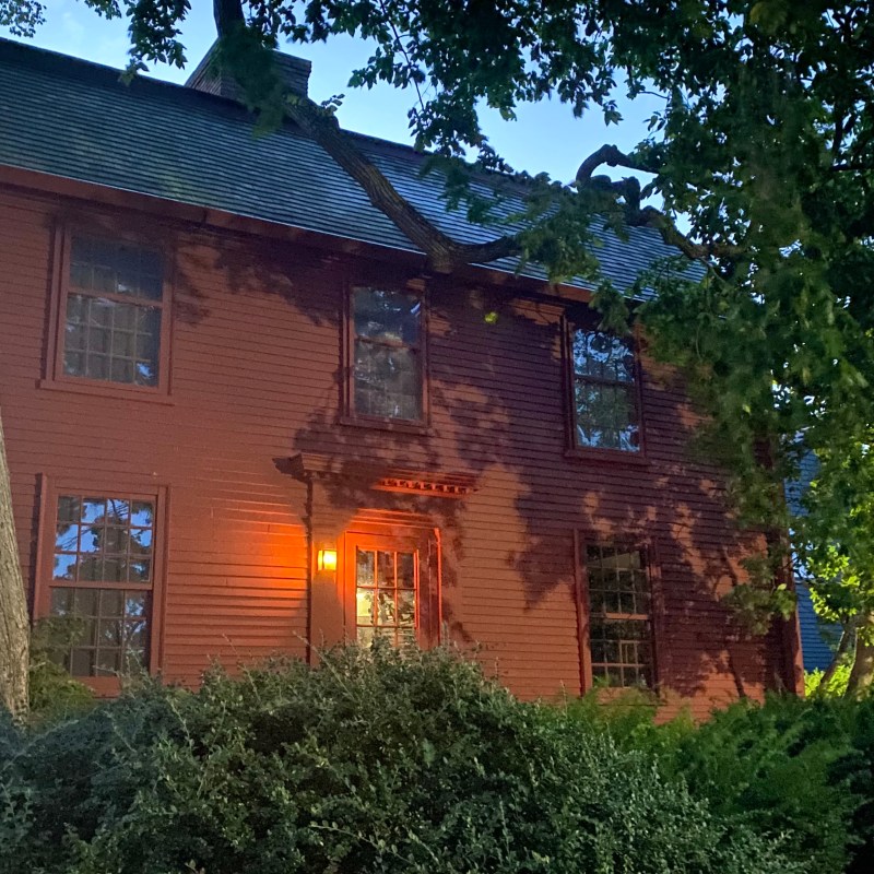 Historic red house at twilight, partially obscured by trees.