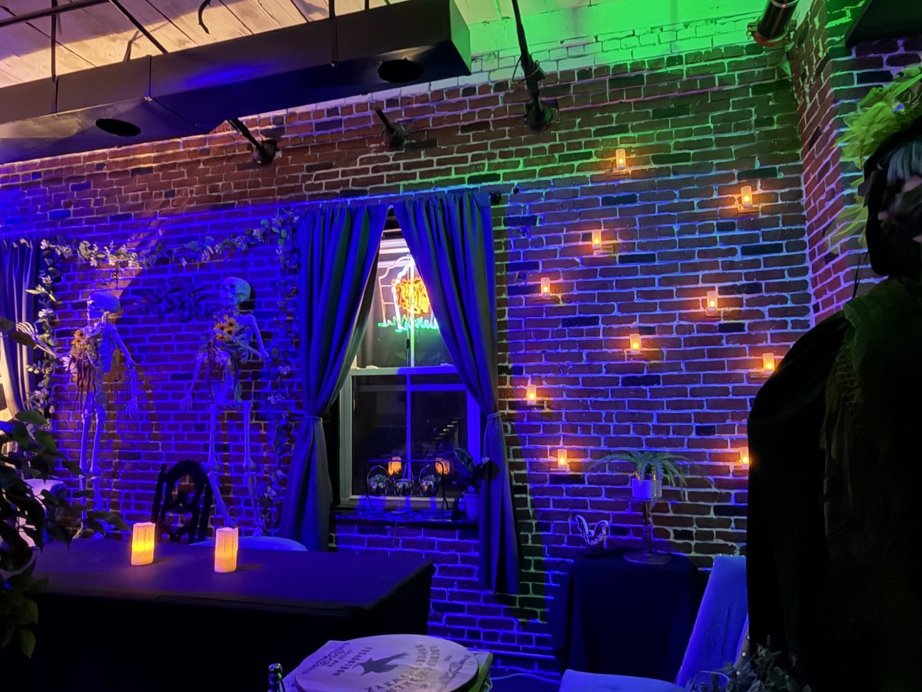 Moody room with brick walls, neon sign, candles, and green-blue lighting.