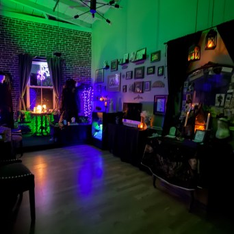 Dimly lit room with green lights, spooky decorations, and a gallery wall.