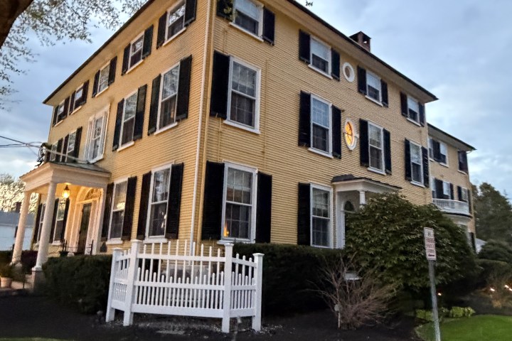 Large three-story yellow house with black shutters and white trim at dusk.